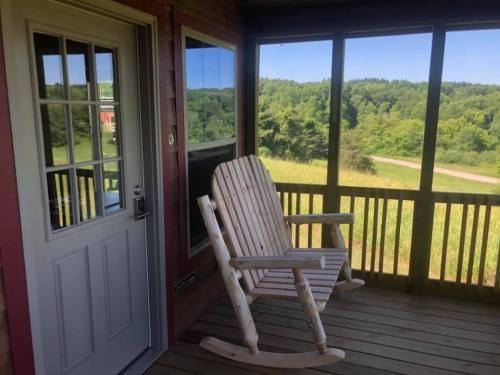 A wooden rocking chair on a porch, overlooking a green landscape and trees in the distance.
