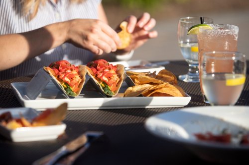 A person enjoys tacos with fresh toppings and crispy chips, accompanied by drinks on a table outdoors.