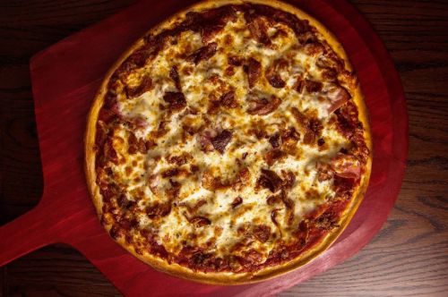 A freshly baked pizza topped with melted cheese and various meats, placed on a wooden pizza peel.