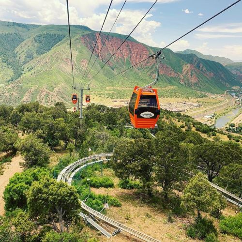 A scenic view of a cable car traveling over lush greenery and mountains, with a winding track below.