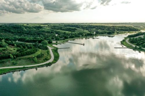 Aerial view of a serene lake surrounded by lush greenery and rolling hills under a cloudy sky.