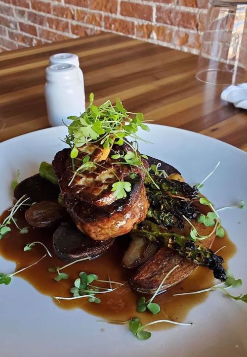 A beautifully plated dish featuring a meat cut topped with microgreens, served with roasted vegetables and sauce.