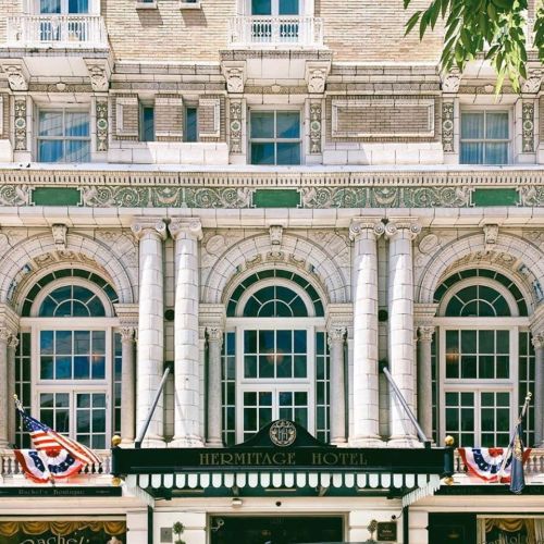 Facade of the Hermitage Hotel featuring ornate columns, large windows, and American flags.