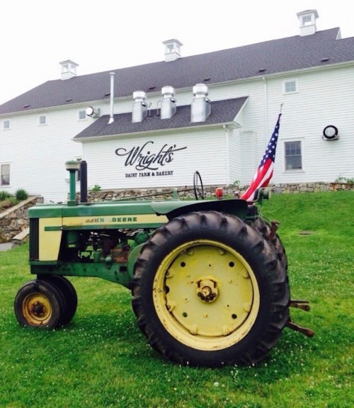A green and yellow tractor with an American flag parked in front of a white barn with "Wright's Dairy Farm & Bakery" sign.