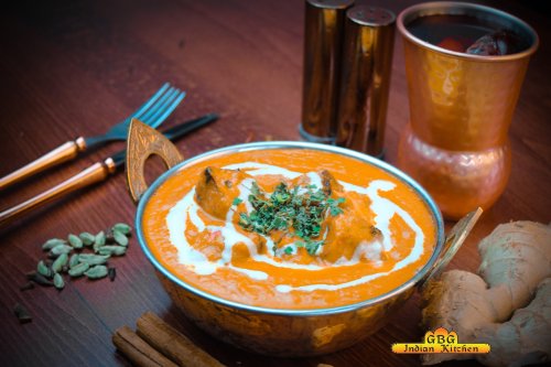 A bowl of creamy orange curry garnished with herbs, surrounded by spices and utensils on a wooden table.