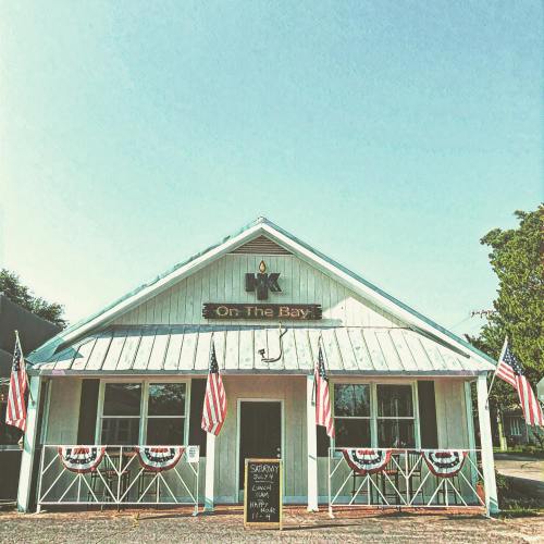 A charming building with a sign reading "On The Bay," decorated with American flags and bunting. Clear blue sky above.