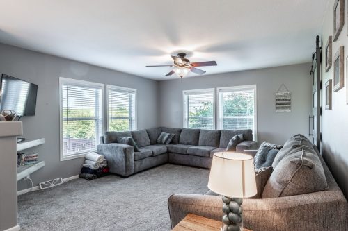 Cozy living room with a large sectional sofa, ceiling fan, and bright windows, featuring a TV and decorative accents.