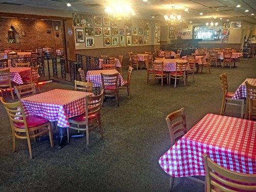 A spacious restaurant with checkered tablecloths, wooden chairs, and framed photos on the walls. Warm lighting creates a cozy atmosphere.