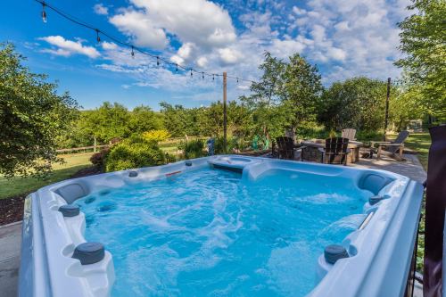 A hot tub with bubbling water, surrounded by greenery and outdoor seating under a blue sky with scattered clouds.
