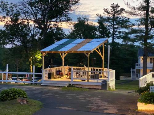 A wooden stage with a colorful roof, surrounded by trees and a pathway, set for an outdoor event at dusk.