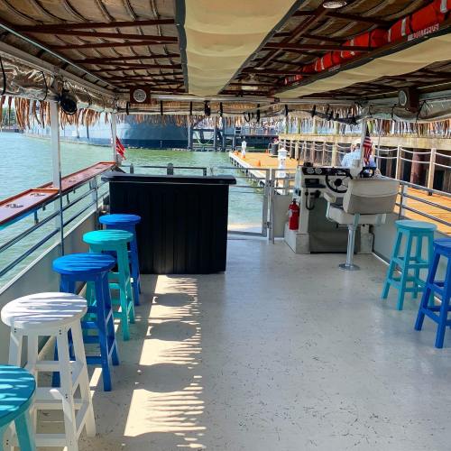 Interior of a boat with colorful stools, a bar area, and a view of the water and dock outside.