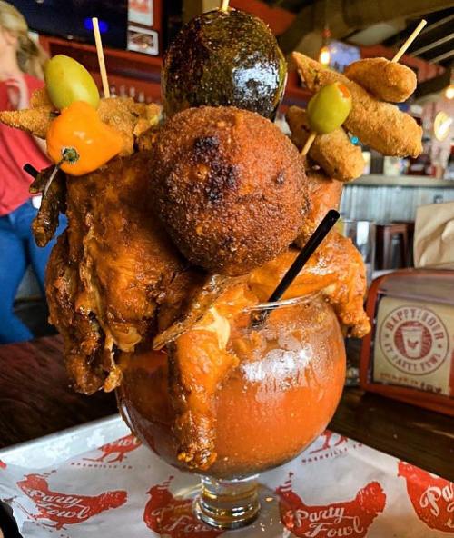 A large cocktail glass filled with a Bloody Mary, topped with fried chicken, olives, and other garnishes.
