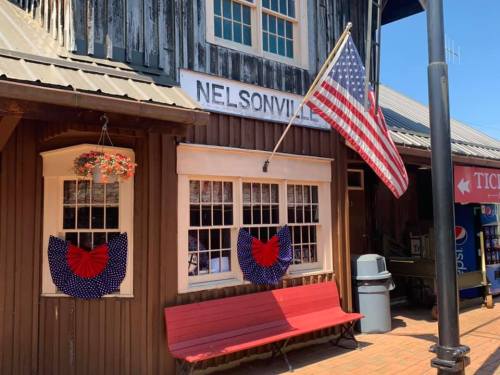A rustic building with a sign reading "Nelsonville," featuring American flags and red, white, and blue decorations.