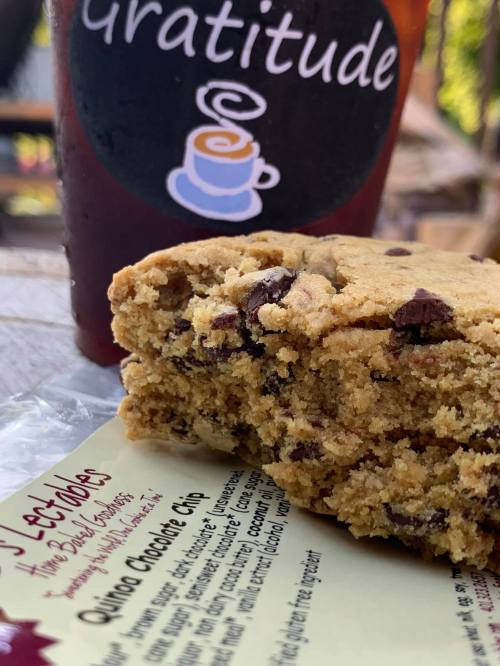 A close-up of a chocolate chip cookie with a bite taken out, next to a drink labeled "Gratitude."
