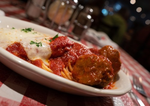 A plate of spaghetti topped with marinara sauce, meatballs, and melted cheese, served on a checkered tablecloth.