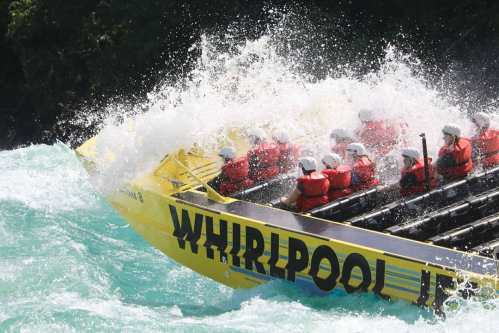 A yellow raft with passengers in life jackets splashes through turbulent turquoise waters.