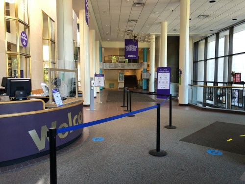 Interior of a welcoming lobby with a reception desk, stanchions, and informational signs. Bright and spacious atmosphere.