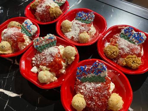 Six red bowls filled with ice cream, cookie dough, and colorful toppings resembling festive desserts.