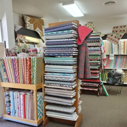 A fabric store interior featuring shelves stacked with colorful rolls of fabric and a cozy, inviting atmosphere.