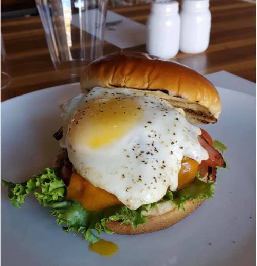 A juicy burger with lettuce, tomato, cheddar cheese, and a sunny-side-up egg on a toasted bun, served on a plate.