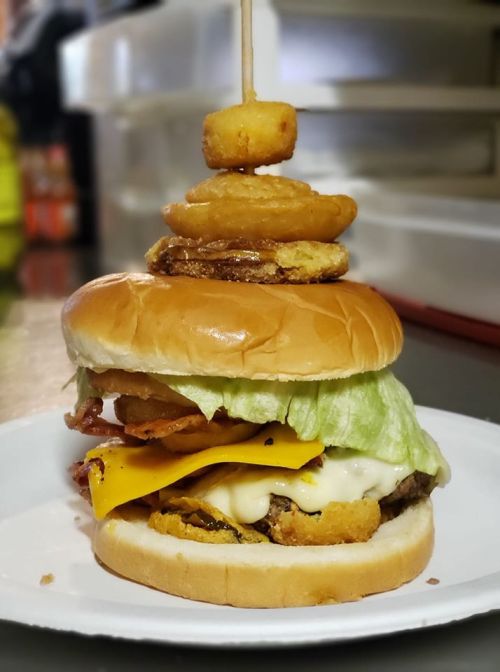 A towering burger with lettuce, cheese, bacon, and crispy onion rings, served on a plate.