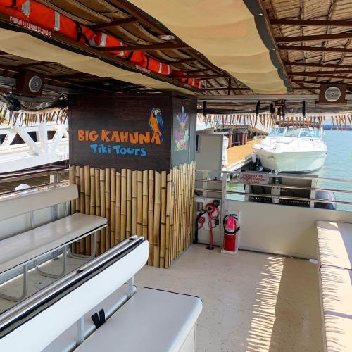 Interior of a tiki tour boat featuring bamboo decor and seating, with a sign for "Big Kahuna Tiki Tours."