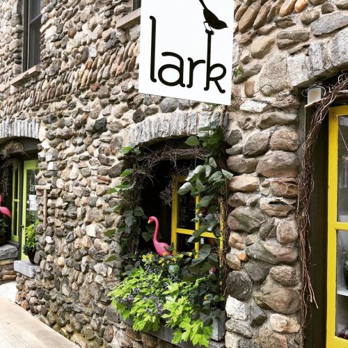 A stone building with a sign reading "lark" and a window adorned with greenery and pink flamingo decorations.