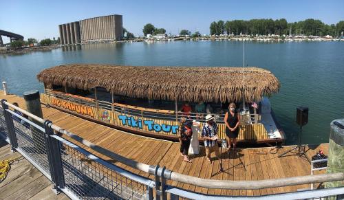 A tiki boat named "Big Kahuna" docked at a marina, with people preparing for a tour on a sunny day.