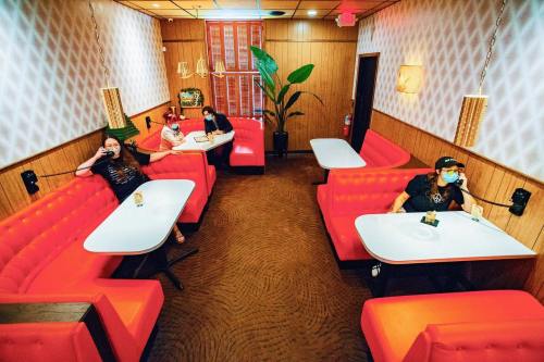 A retro diner with red booths and tables, featuring four masked patrons sitting apart in a cozy, vintage setting.