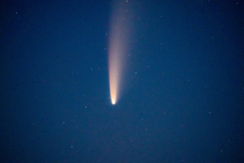 A bright comet with a long tail streaks across a dark night sky filled with stars.