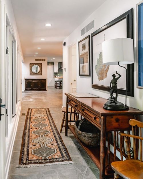 A hallway with a patterned runner rug, wooden console table, and framed artwork on the walls, leading to a mirrored room.