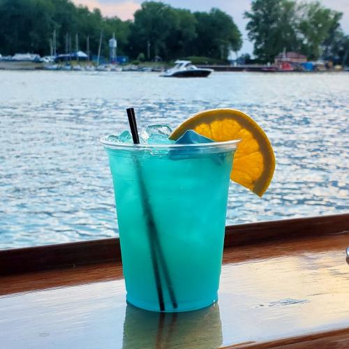 A refreshing blue cocktail with ice and a lemon slice, set against a scenic waterfront view.