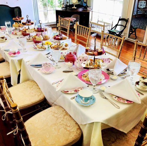 A beautifully set dining table with elegant tea cups, plates of pastries, and floral decorations.
