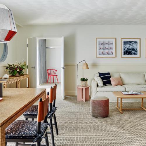 Bright, modern living space featuring a sofa, dining area, and artwork, with an open door leading to another room.