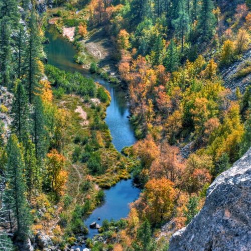 Aerial view of a winding river surrounded by vibrant autumn foliage and rocky terrain.