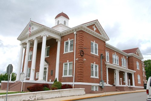 Historic brick building with white columns, a dome, and large windows, set against a cloudy sky.