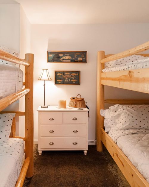 Cozy bedroom with wooden bunk beds, a white dresser, and a lamp, featuring warm lighting and simple decor.