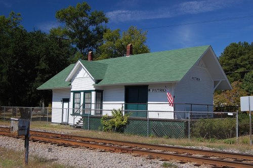 Historic train station with a green roof, white exterior, and an American flag, surrounded by a fence and railway tracks.