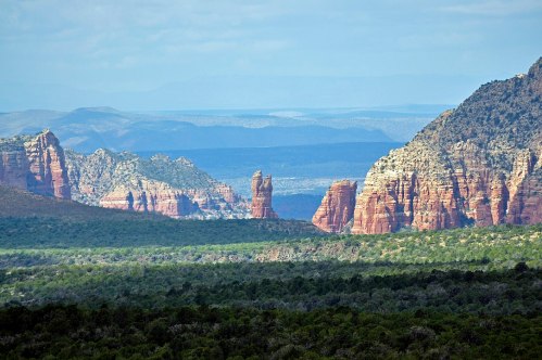 A scenic view of red rock formations and green valleys under a blue sky in a mountainous landscape.
