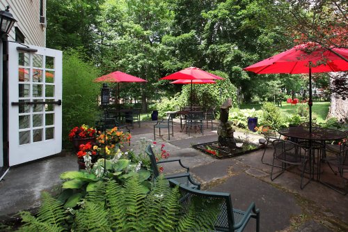 A serene outdoor patio with red umbrellas, surrounded by greenery and colorful flowers, inviting for relaxation.