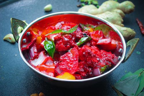 A vibrant bowl of mixed vegetable curry with red beets, herbs, and spices, set against a dark background.
