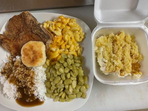 A plate of food featuring fried pork chop, macaroni and cheese, rice with gravy, green beans, a biscuit, and cake.