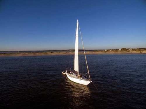 A white sailboat with a tall mast sailing on calm blue waters under a clear sky.