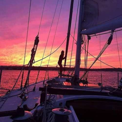 A silhouette of a person on a sailboat against a vibrant pink and purple sunset over the water.