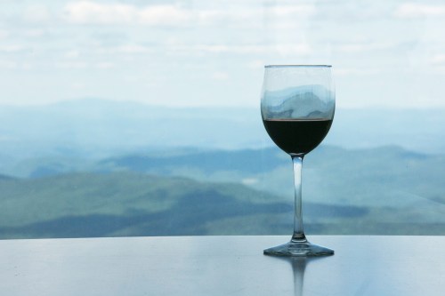 A glass of wine sits on a table with a scenic mountain view in the background.