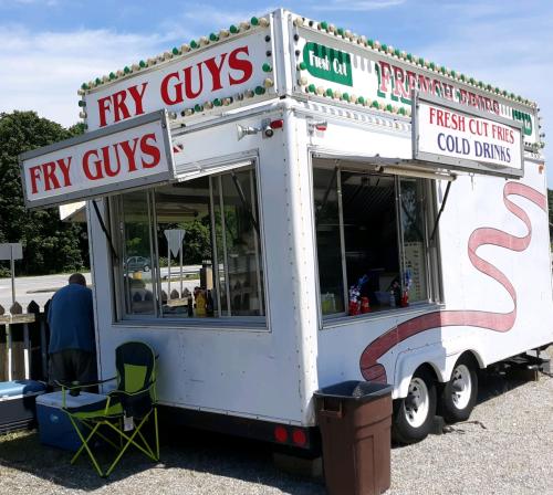 A food truck named "Fry Guys" serving fresh cut fries and cold drinks, parked by a roadside with a customer nearby.