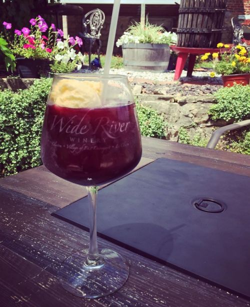 A glass of red wine with a scoop of ice cream, set on a wooden table surrounded by colorful flowers.