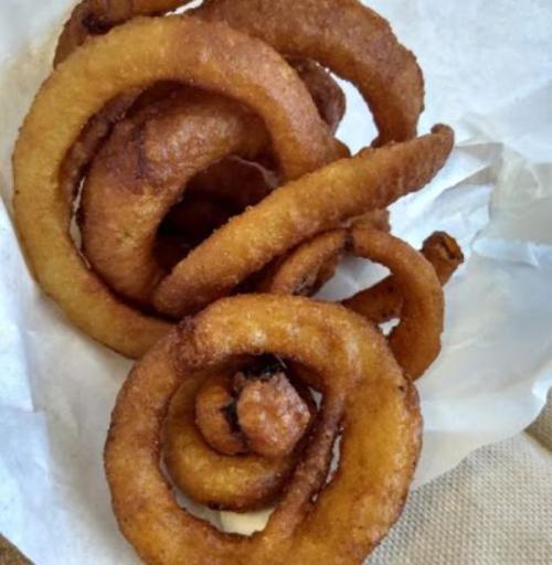 A pile of golden-brown, crispy onion rings arranged in spirals on a white paper background.