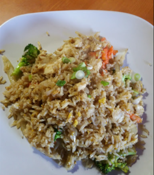 A plate of fried rice mixed with vegetables, including broccoli and carrots, garnished with green onions.