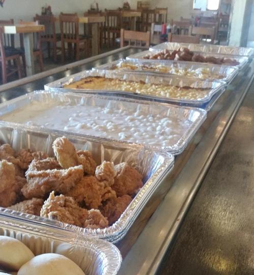 A buffet table with trays of fried chicken, creamy dishes, and baked goods in a casual dining setting.